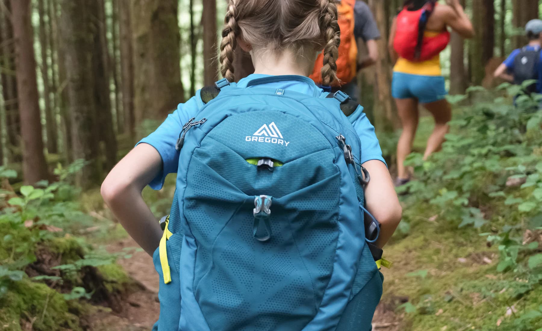 A child wearing a blue backpack on a wooded trail