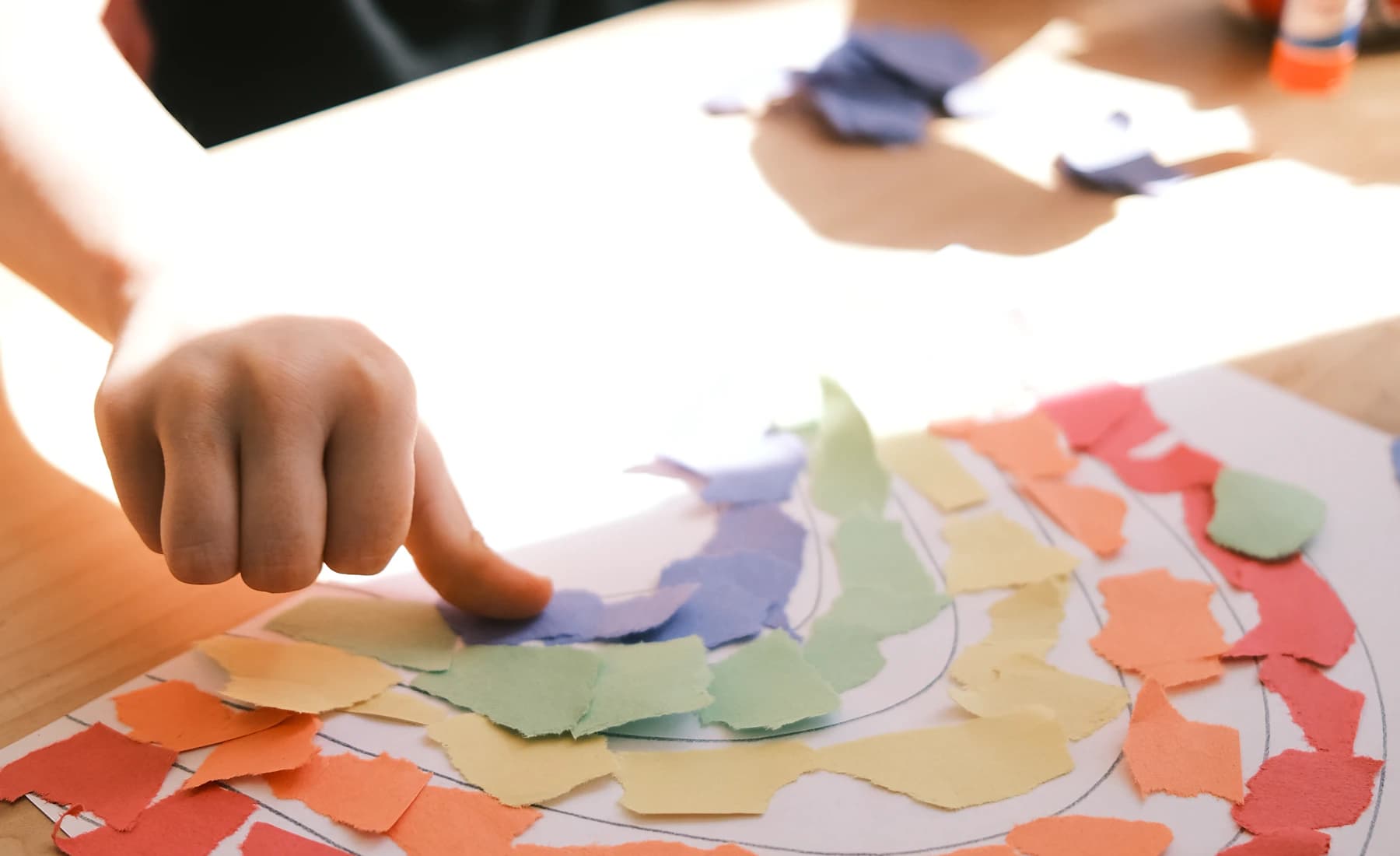 A child making a colorful paper collage at a table