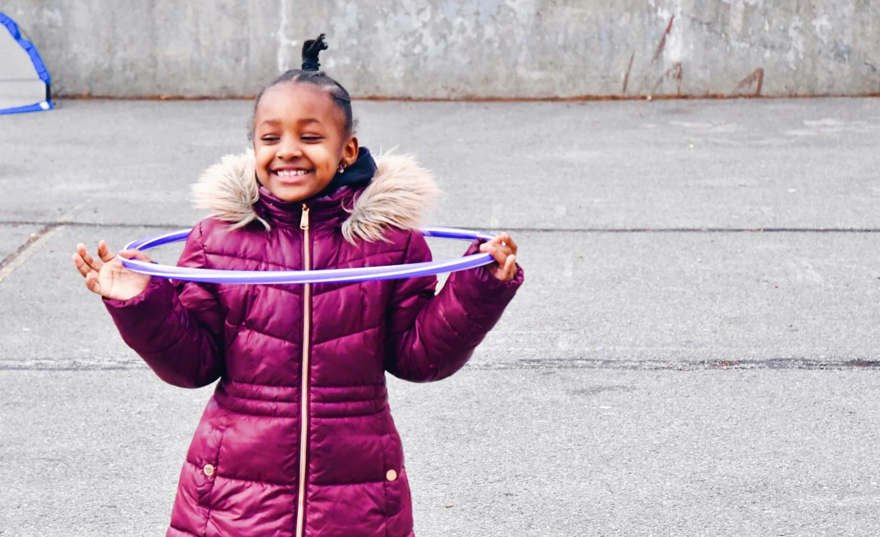 A smiling child holding a hula hoop during an outdoor activity
